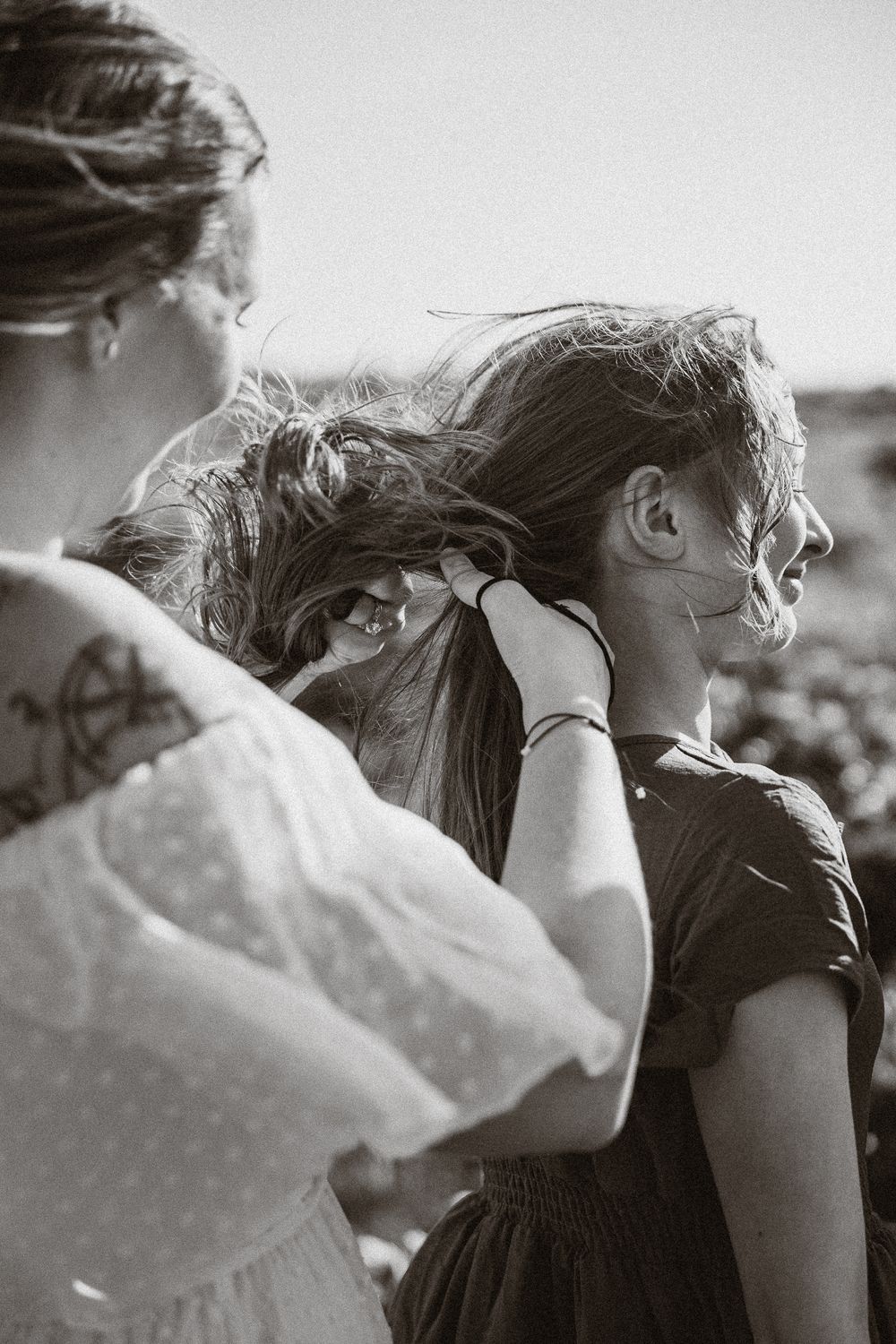 A candid black and white photo showing people with wind-blown hair against a natural backdrop.