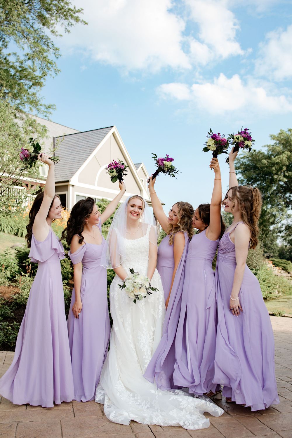 Wedding party in lavender bridesmaid dresses and white bridal gown celebrating outdoors.