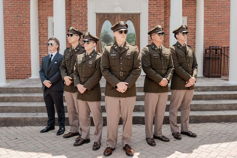 Military personnel in brown uniforms stand in formation outside a brick building.