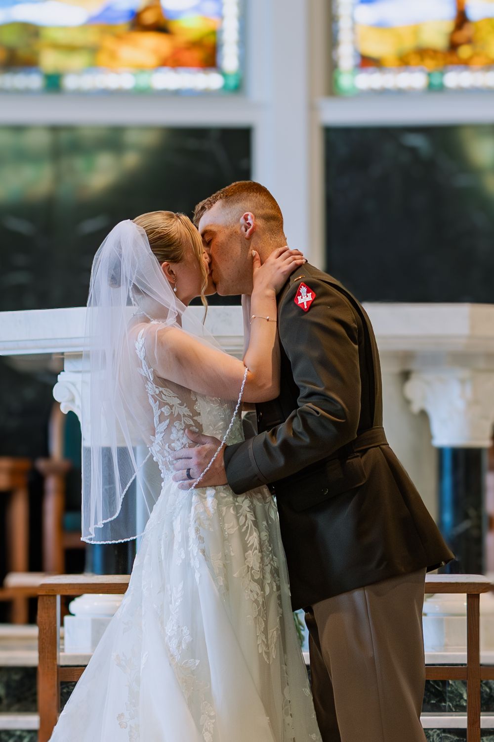 A couple shares a romantic kiss during their wedding ceremony in a bright, sunlit venue.