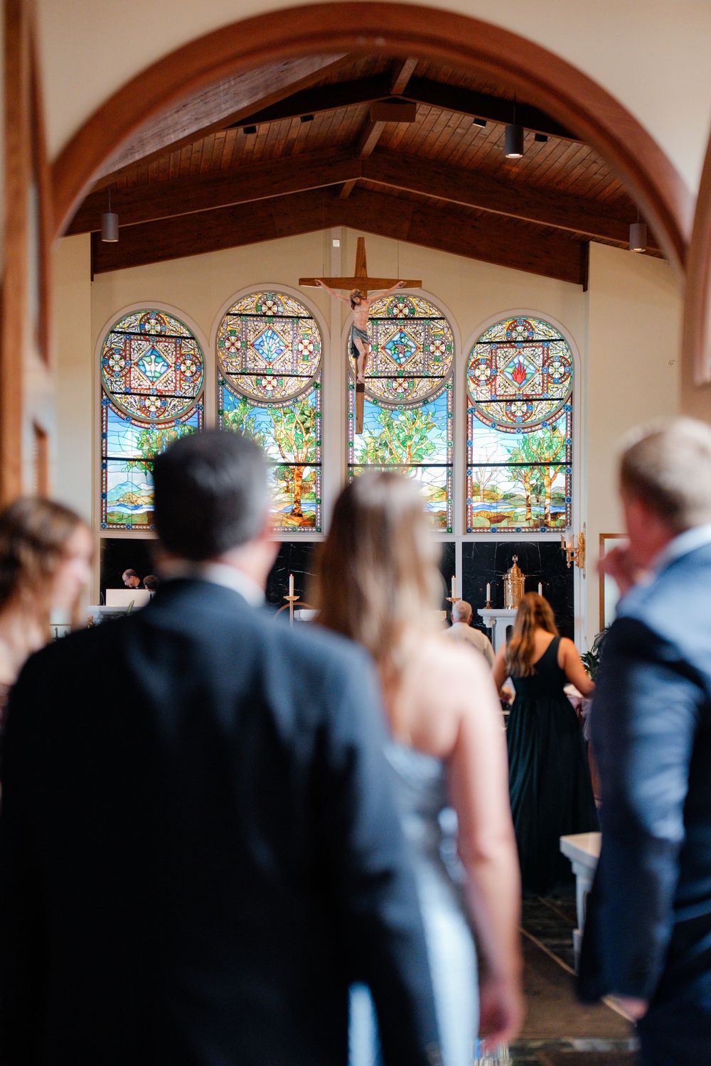 Church interior with stained glass windows and wooden beams during a wedding ceremony.