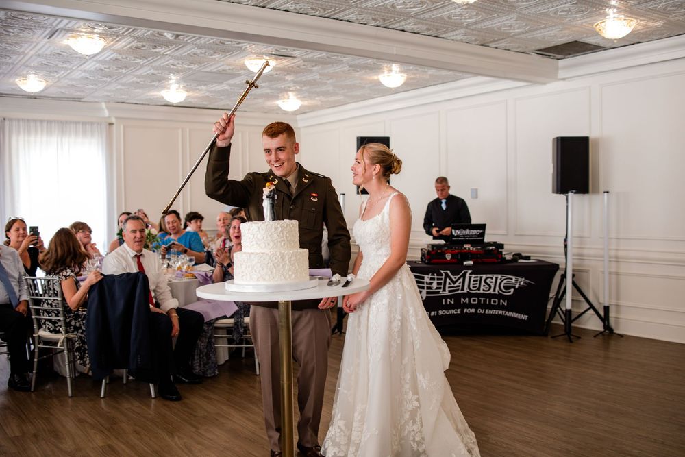 A couple shares their first dance at a wedding reception in a bright indoor venue with guests watching from tables.