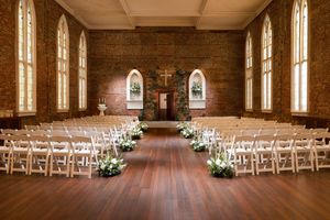 Interior of a brick church with wooden floors and white chairs arranged for a wedding ceremony.