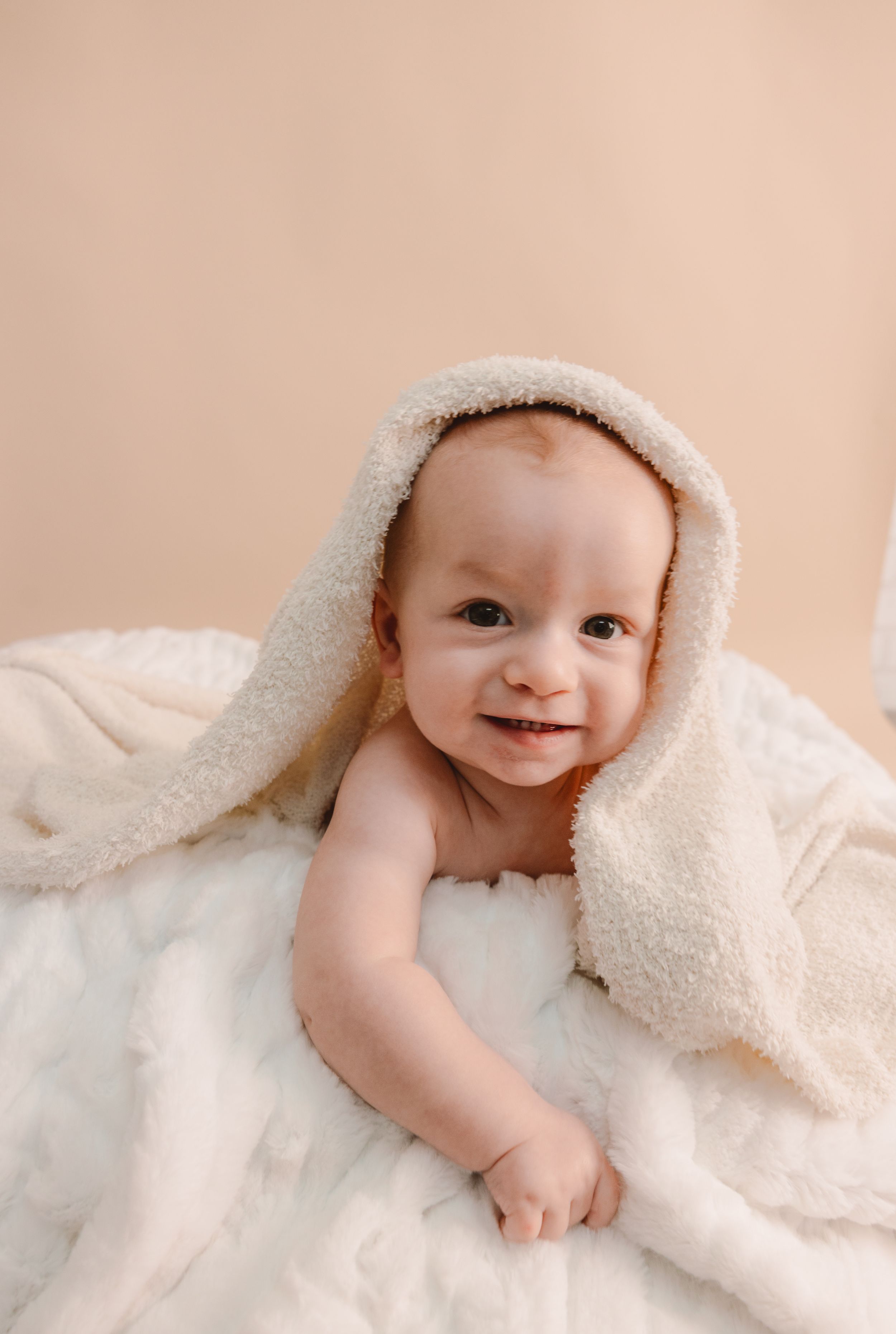 A series of sweet baby photos showing a little one wrapped in a soft cream-colored blanket against a neutral background.