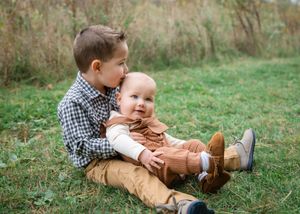 Two children in casual clothing playing together on grassy ground during autumn season.