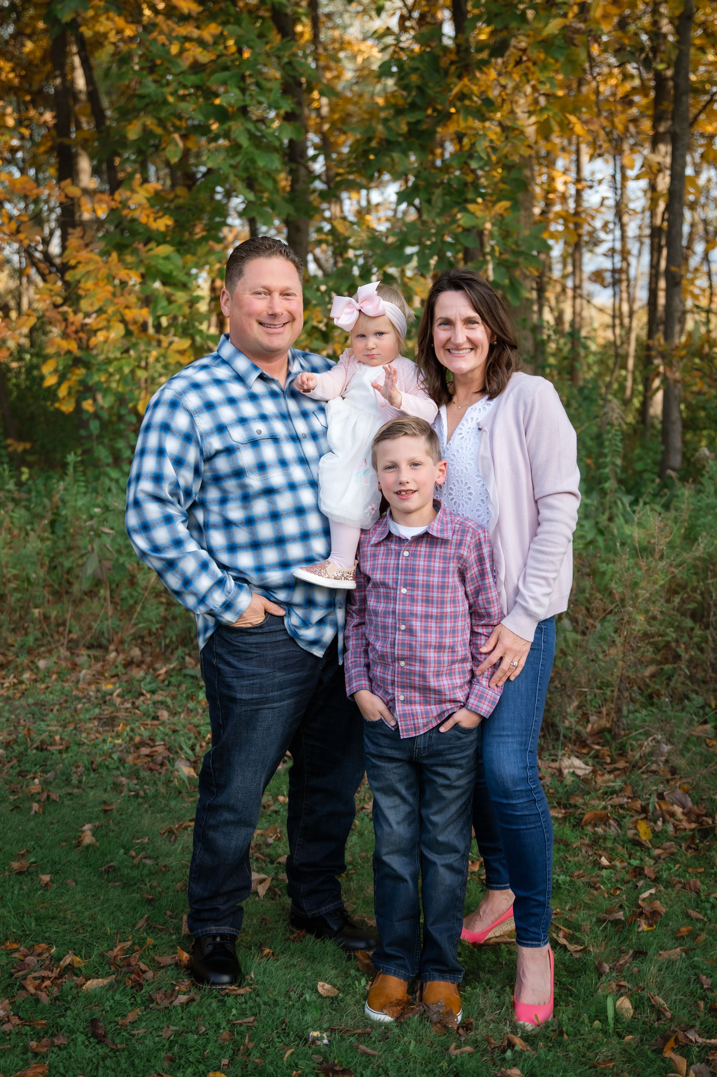 A family poses together in an autumn forest setting with golden leaves and trees in the background.