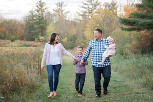 Family walks together holding hands through an autumn field with evergreen trees in the background.