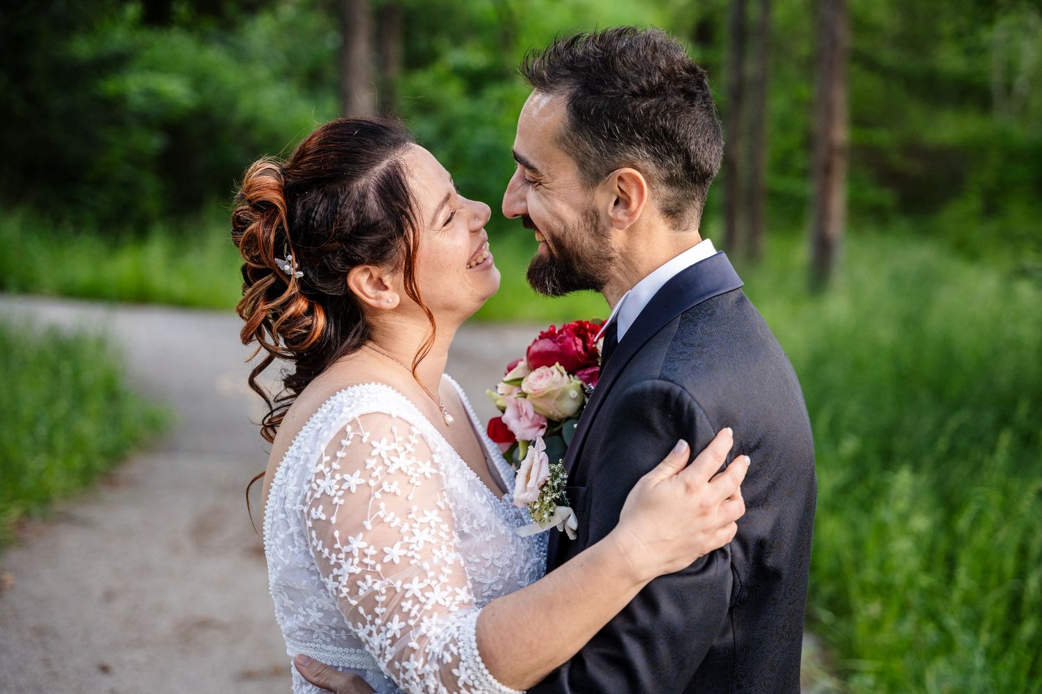 A wedding couple poses together in a scenic mountain meadow with wildflowers and green grass under blue skies.