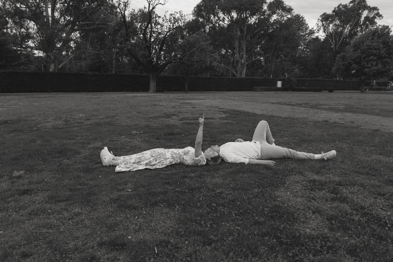 A couple lovingly laying together in the grass pointing up at the sky.