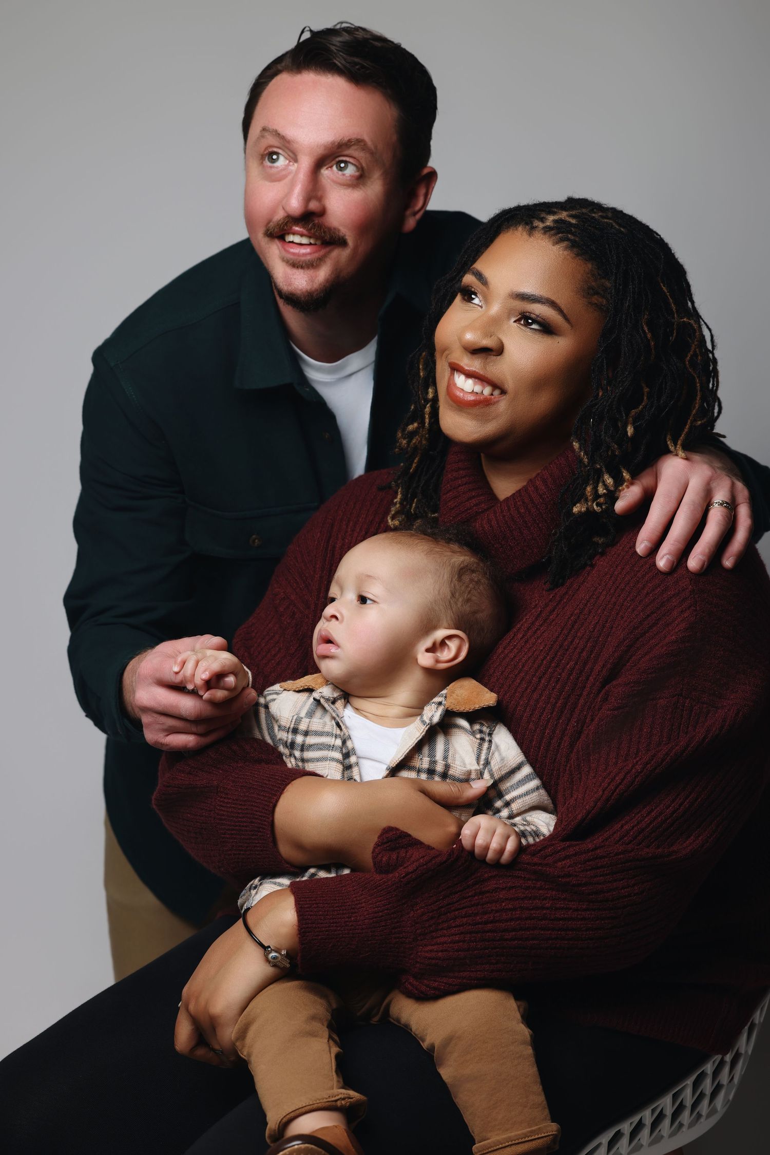 A family in coordinated burgundy and black outfits poses together in a studio against a light gray background.