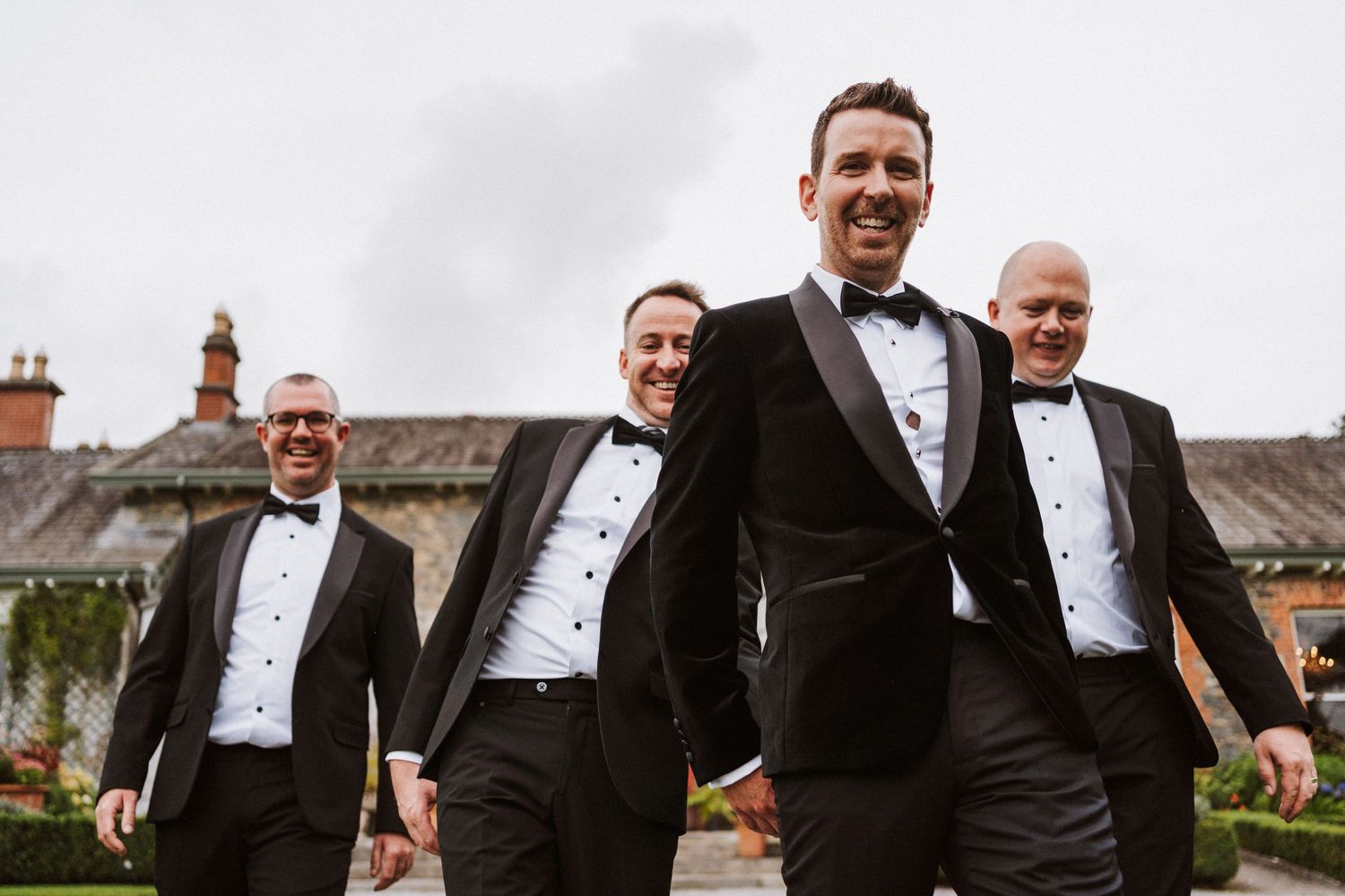 A group in formal black tuxedos and bow ties walking and laughing together outdoors.
