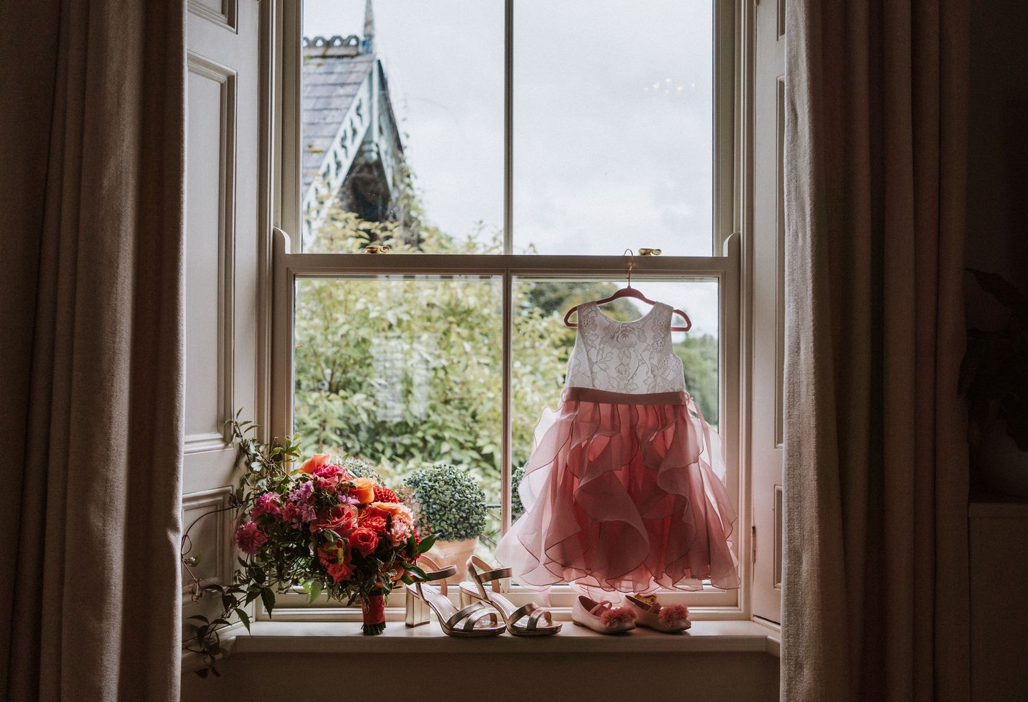 Sunlight streams through vintage windows onto a rustic wooden table with pink and coral flowers in vases.