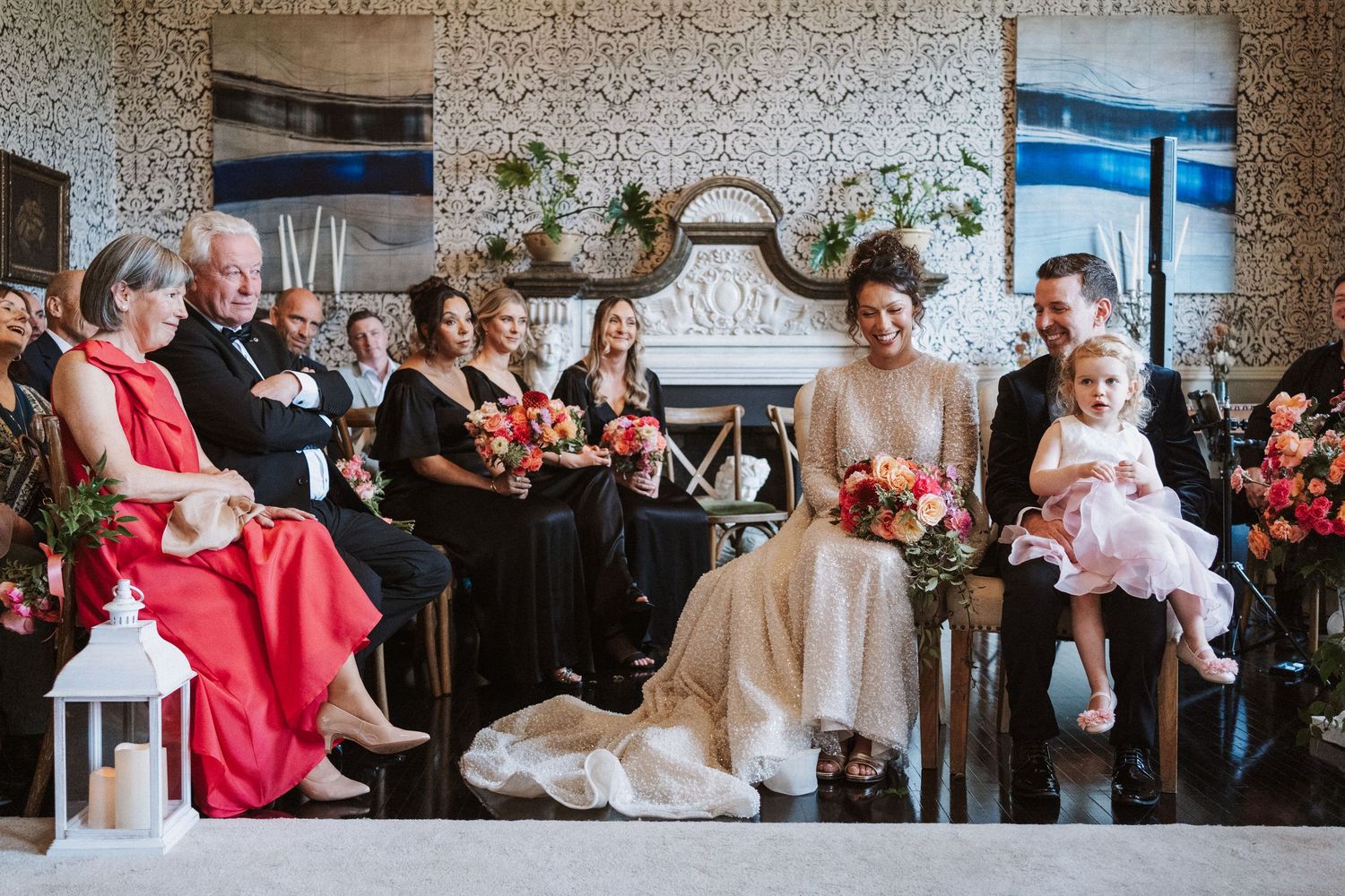 Wedding guests seated in rows at an elegant venue with patterned wallpaper and decorative details.