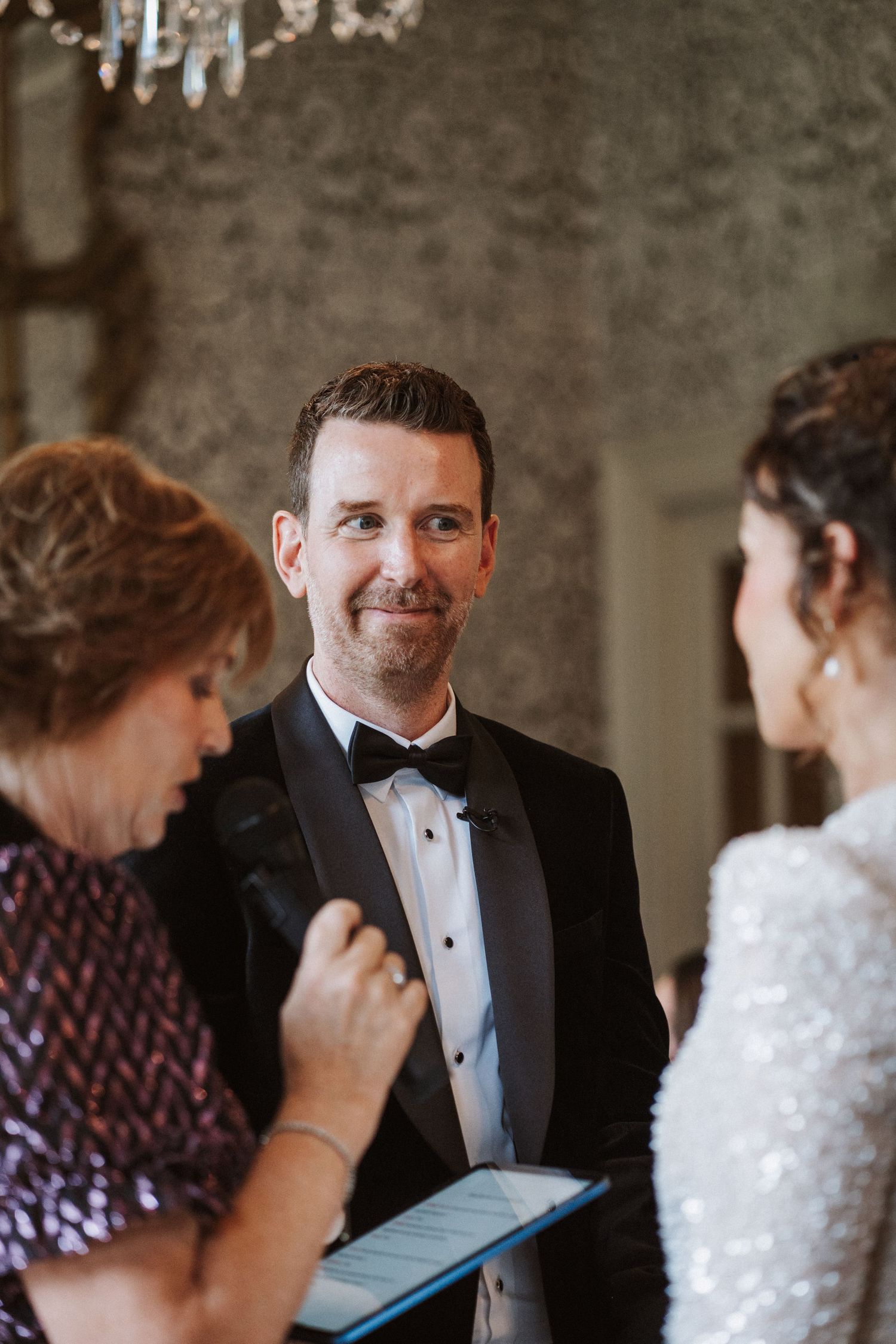 Intimate wedding ceremony moments captured under crystal chandeliers in an ornate room.