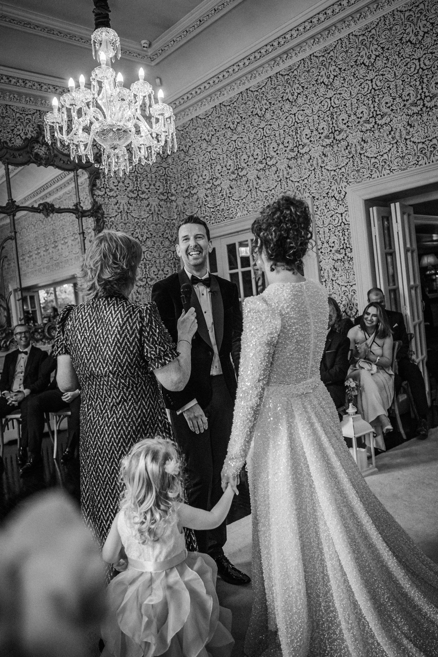 Black and white photos show guests dancing and celebrating at an elegant wedding reception with crystal chandeliers.