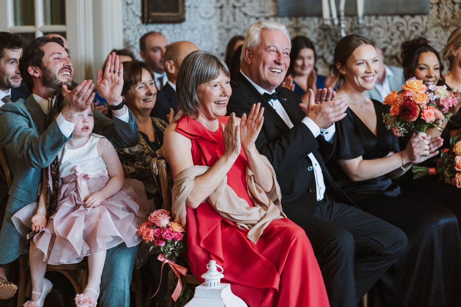 Wedding guests enjoying a celebration in a formal venue with red dresses and floral decorations.