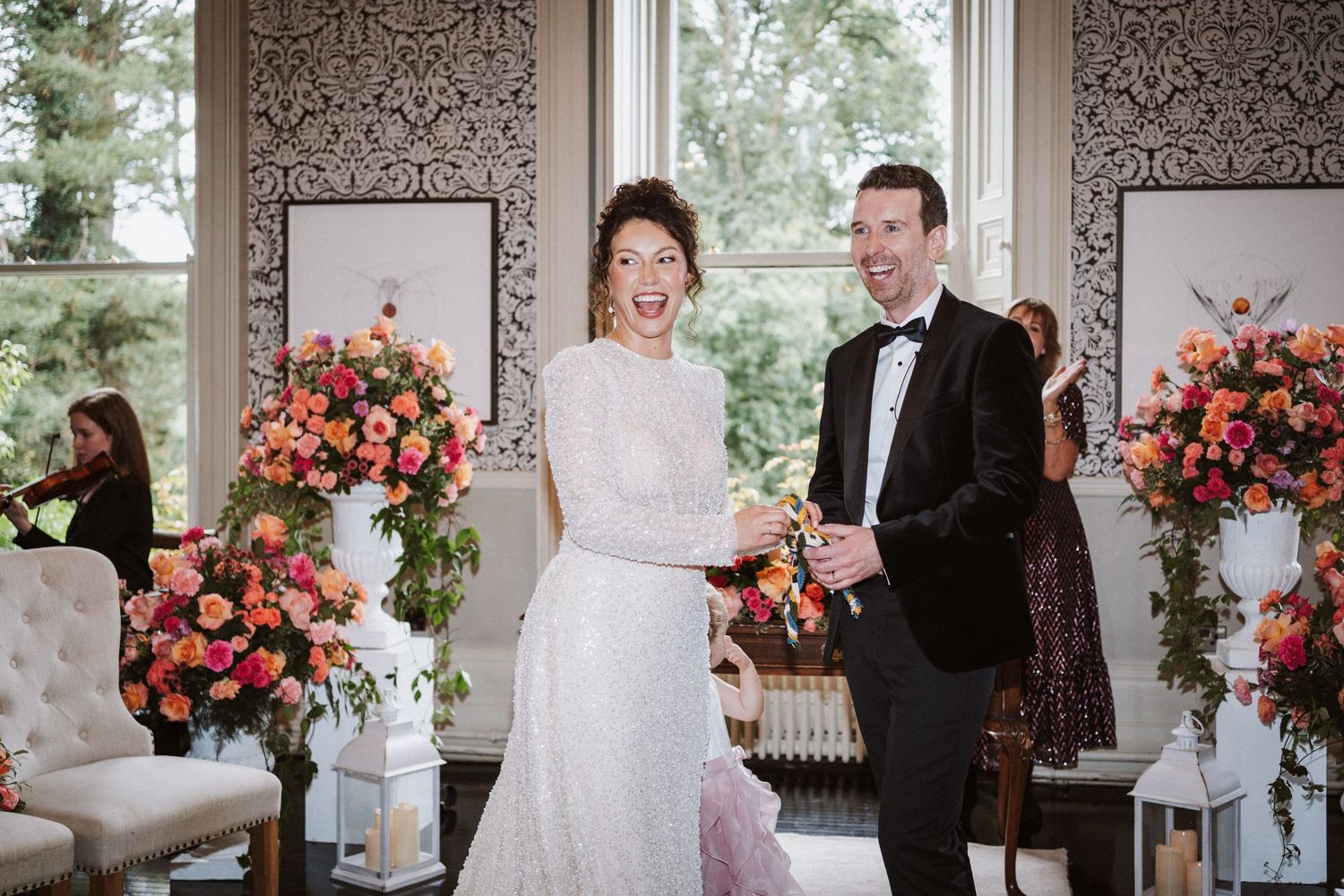A couple shares a joyful moment surrounded by elegant floral arrangements at their wedding celebration.