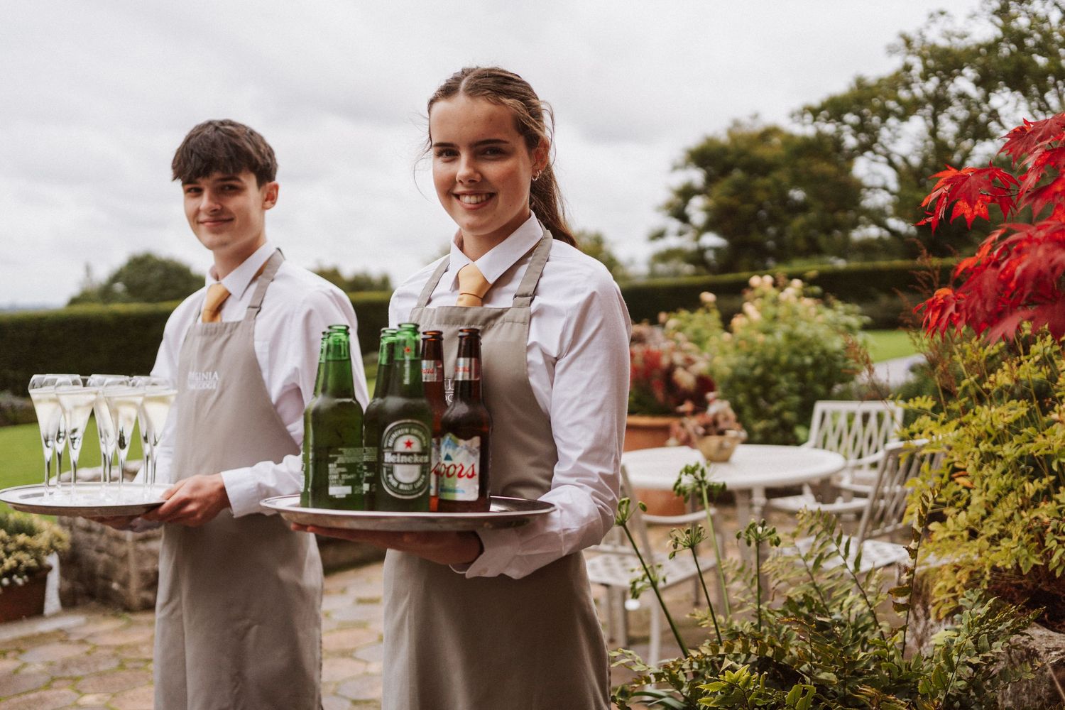 Waitstaff carrying drinks and appetizers on serving trays at an outdoor garden party event.