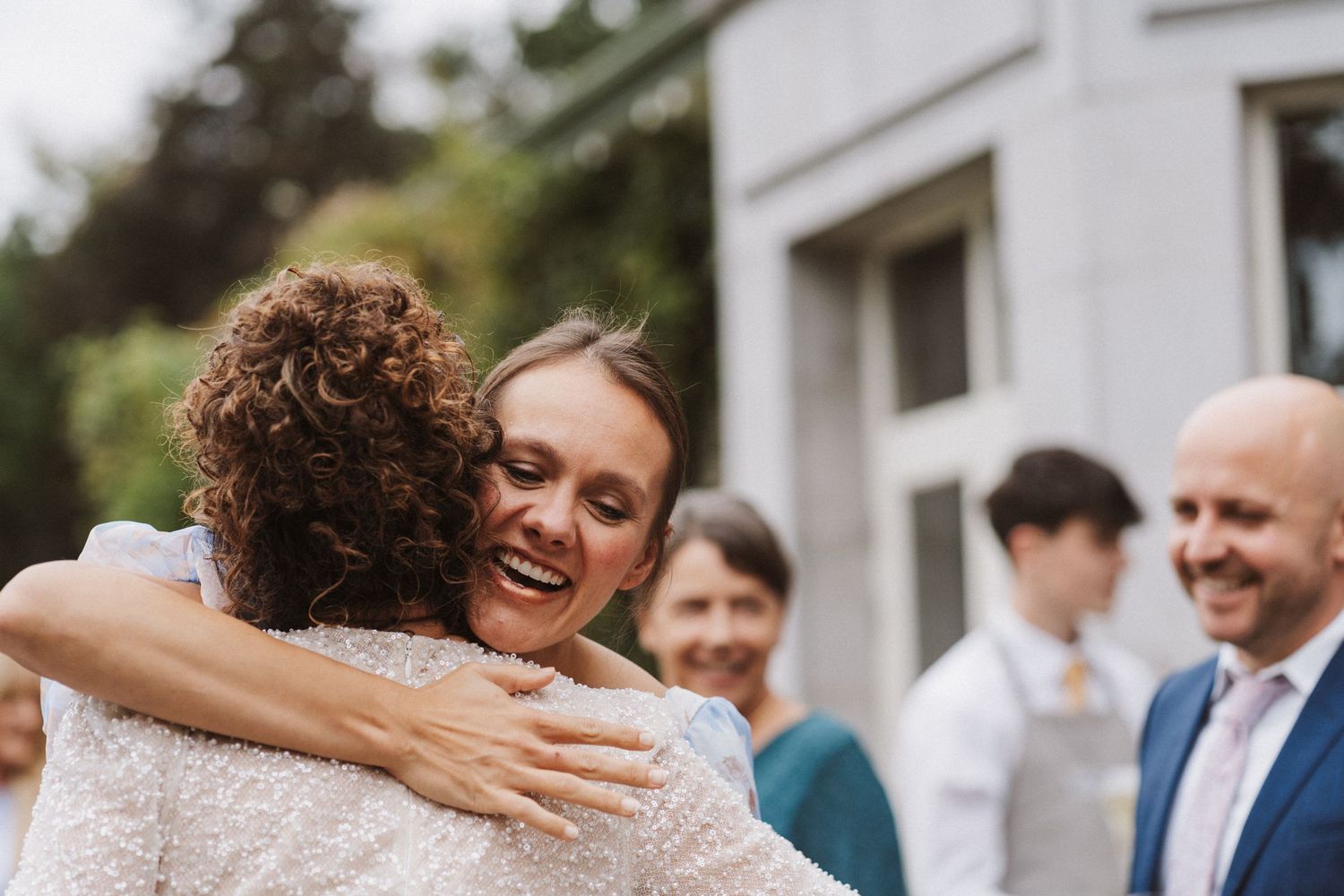 Wedding guests embrace and share joyful moments during outdoor reception celebration.