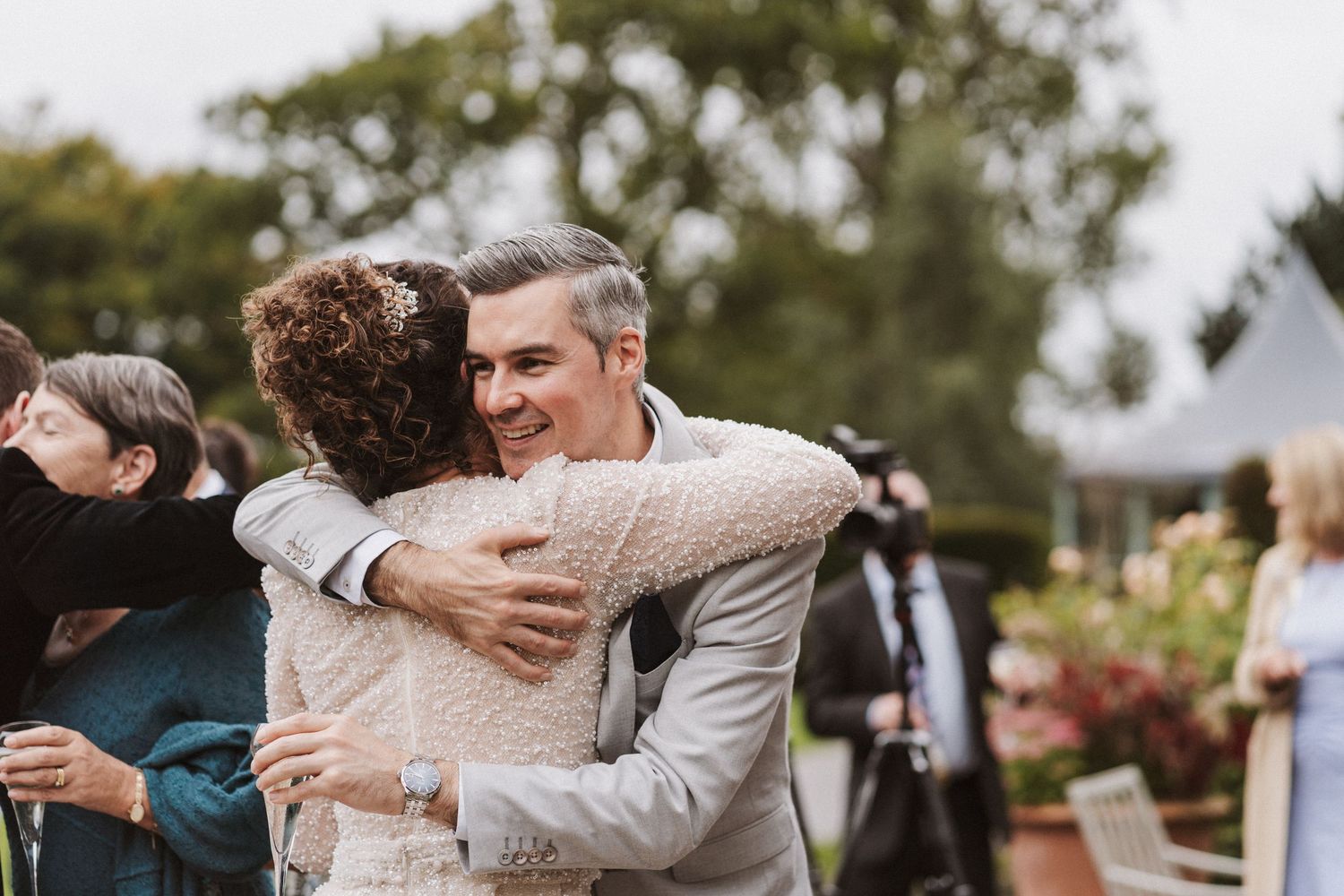 Couple embraces during emotional outdoor wedding celebration with guests looking on in natural setting.