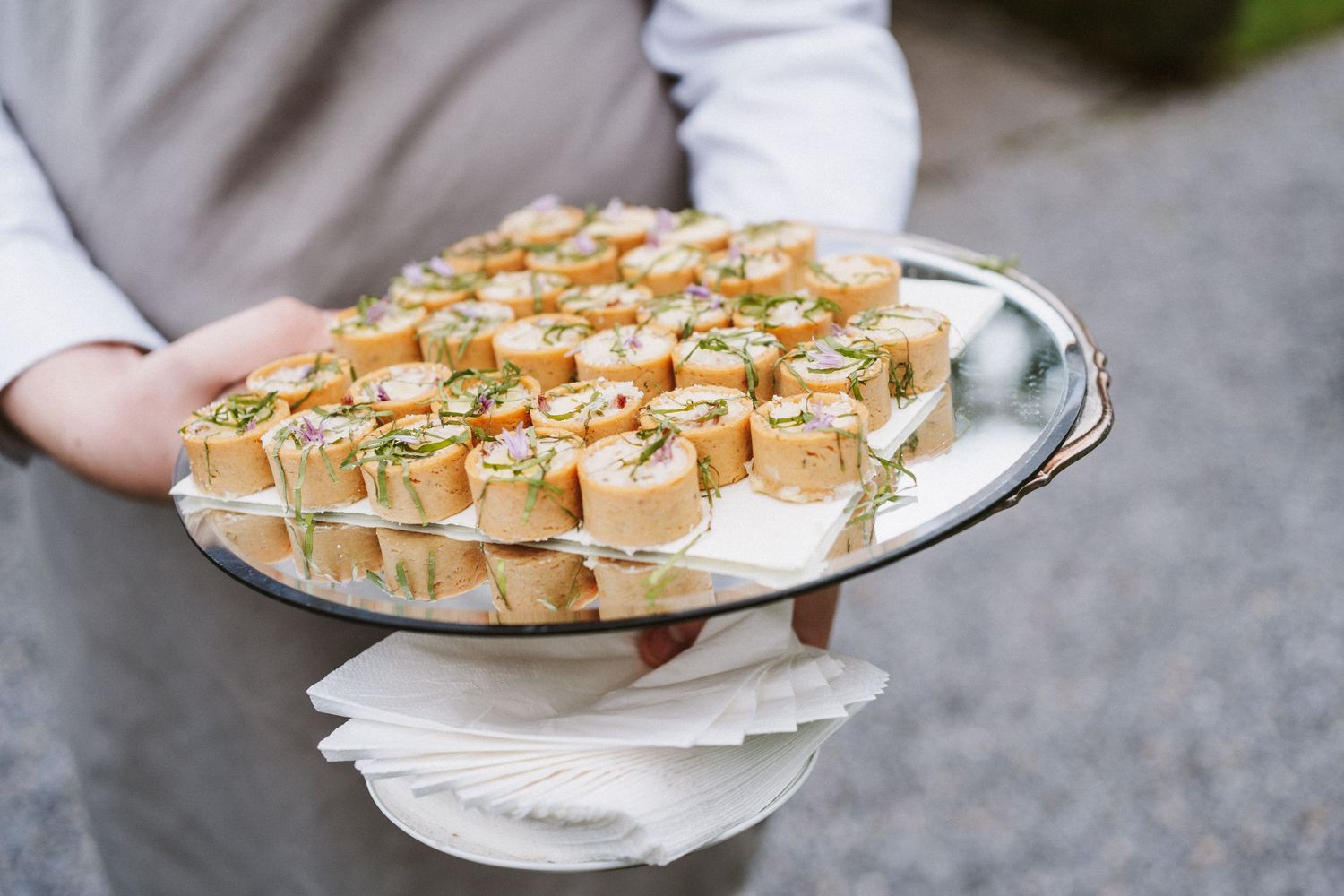 Hands holding plates of mini quiche appetizers garnished with fresh herbs and nuts.