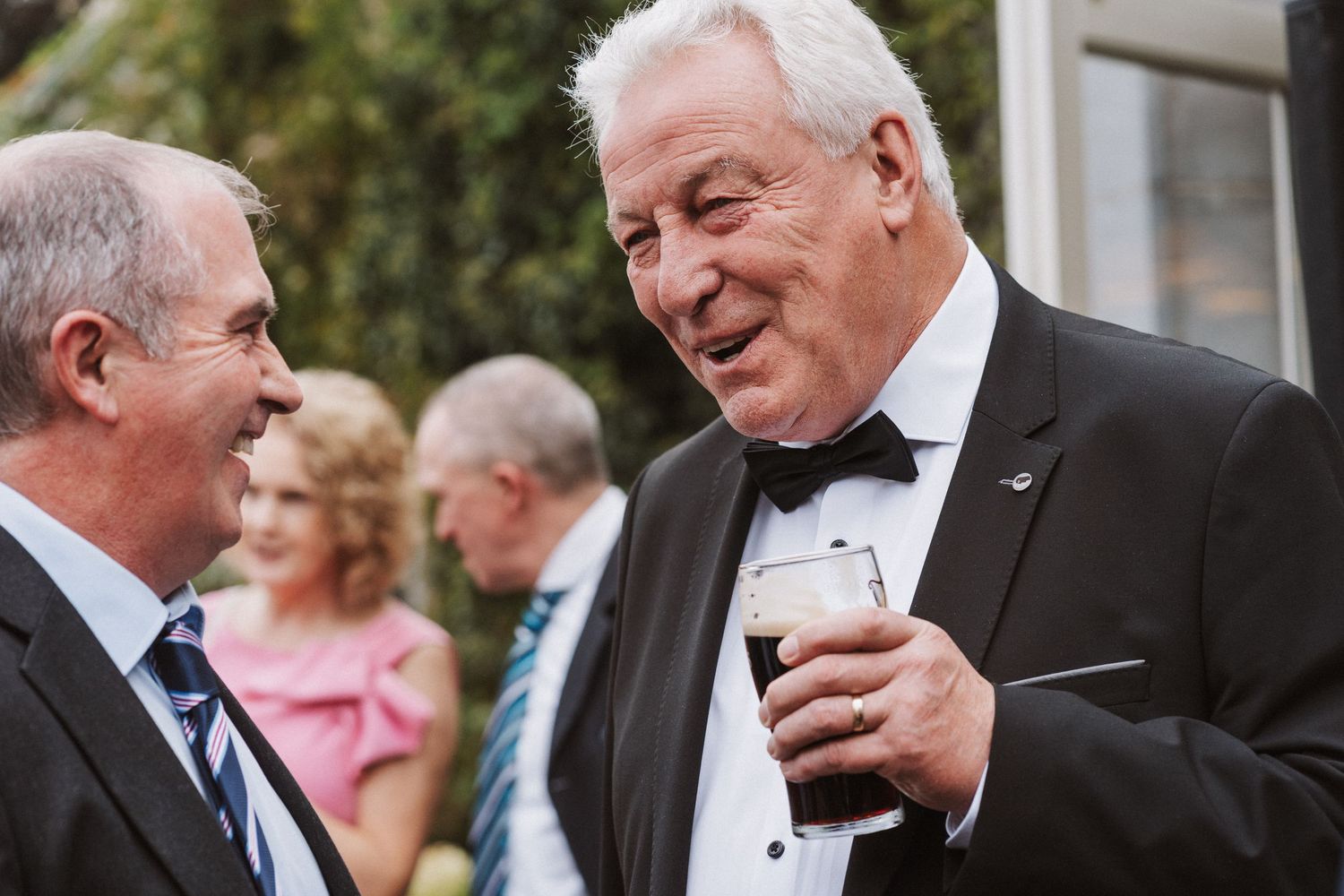 Wedding guests share laughter and conversation during an outdoor cocktail reception.