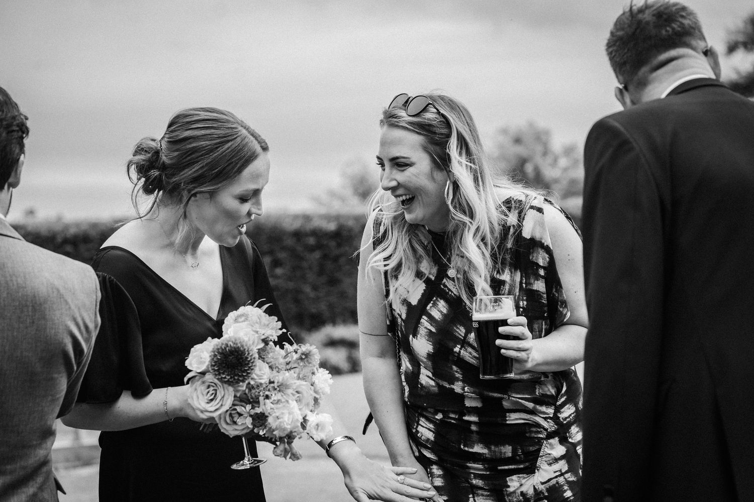 Black and white candid photo of guests mingling and holding drinks at an outdoor wedding reception.