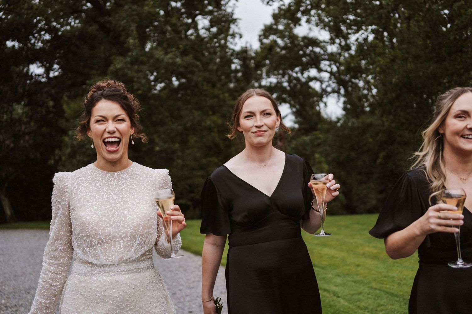 Wedding party members laugh and celebrate outdoors on a sunny day.