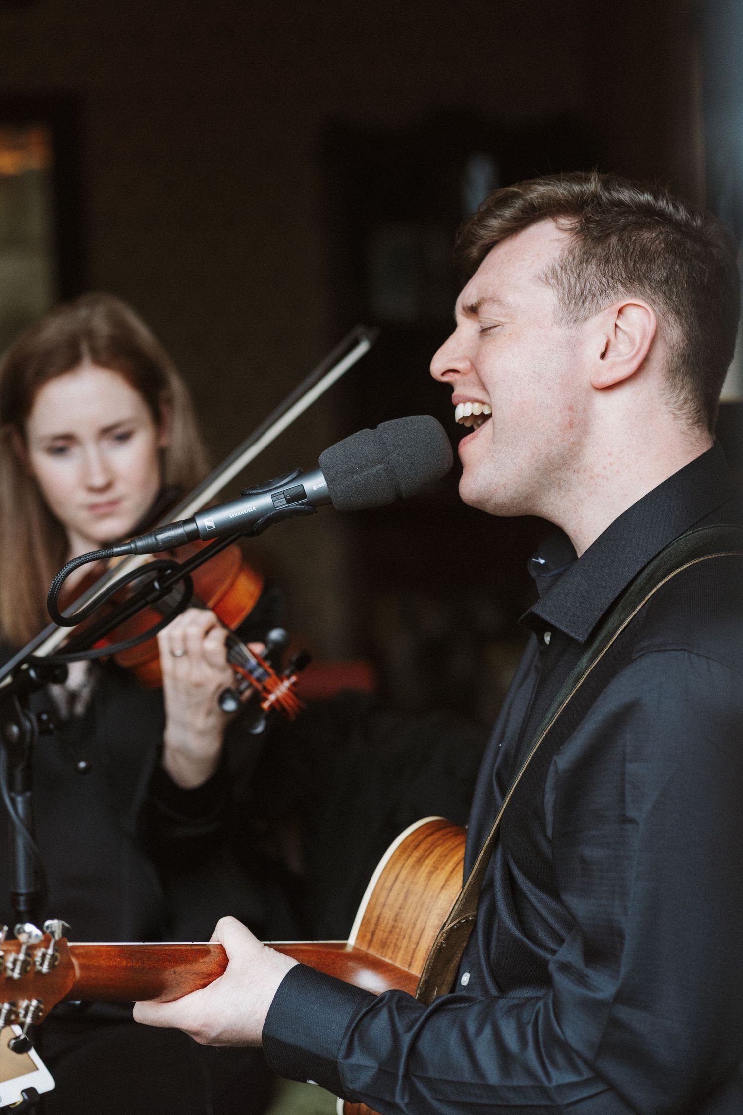 Musicians in black suits perform with acoustic instruments and microphones during a live performance.