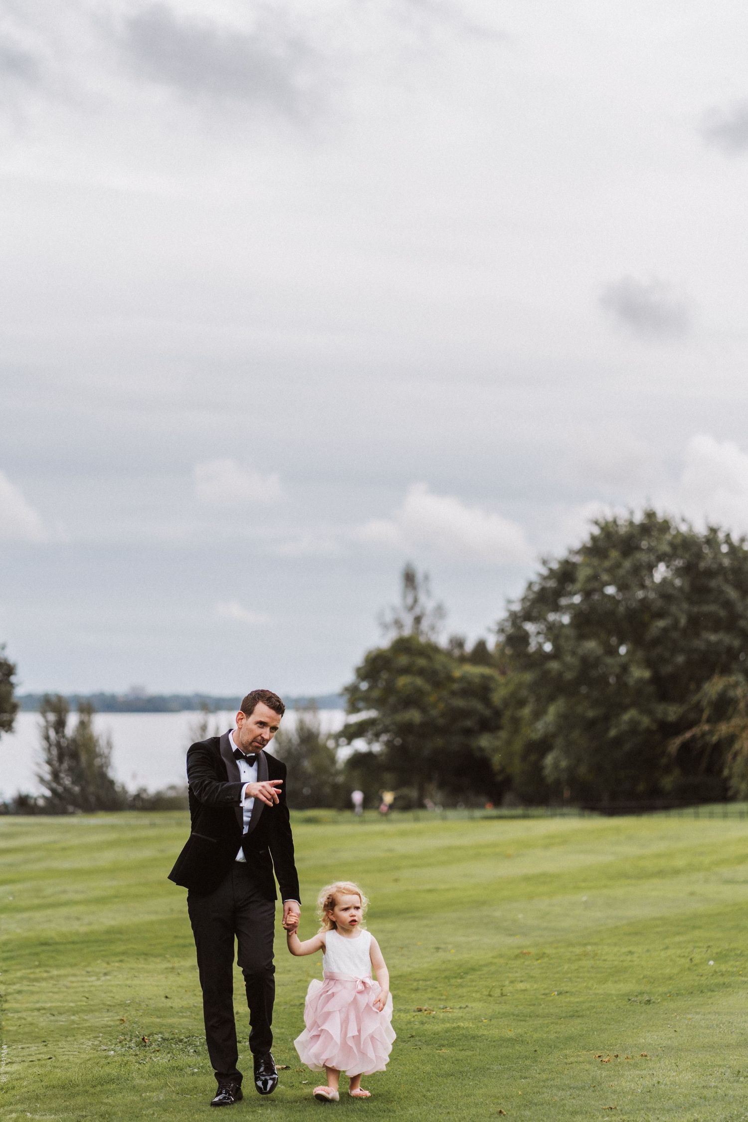 A scenic lakeside lawn setting shows two figures enjoying a special moment together on the green grass.