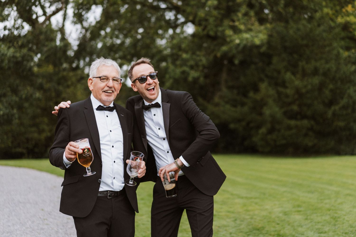 Wedding party in formal attire enjoying candid moments together on a green lawn.