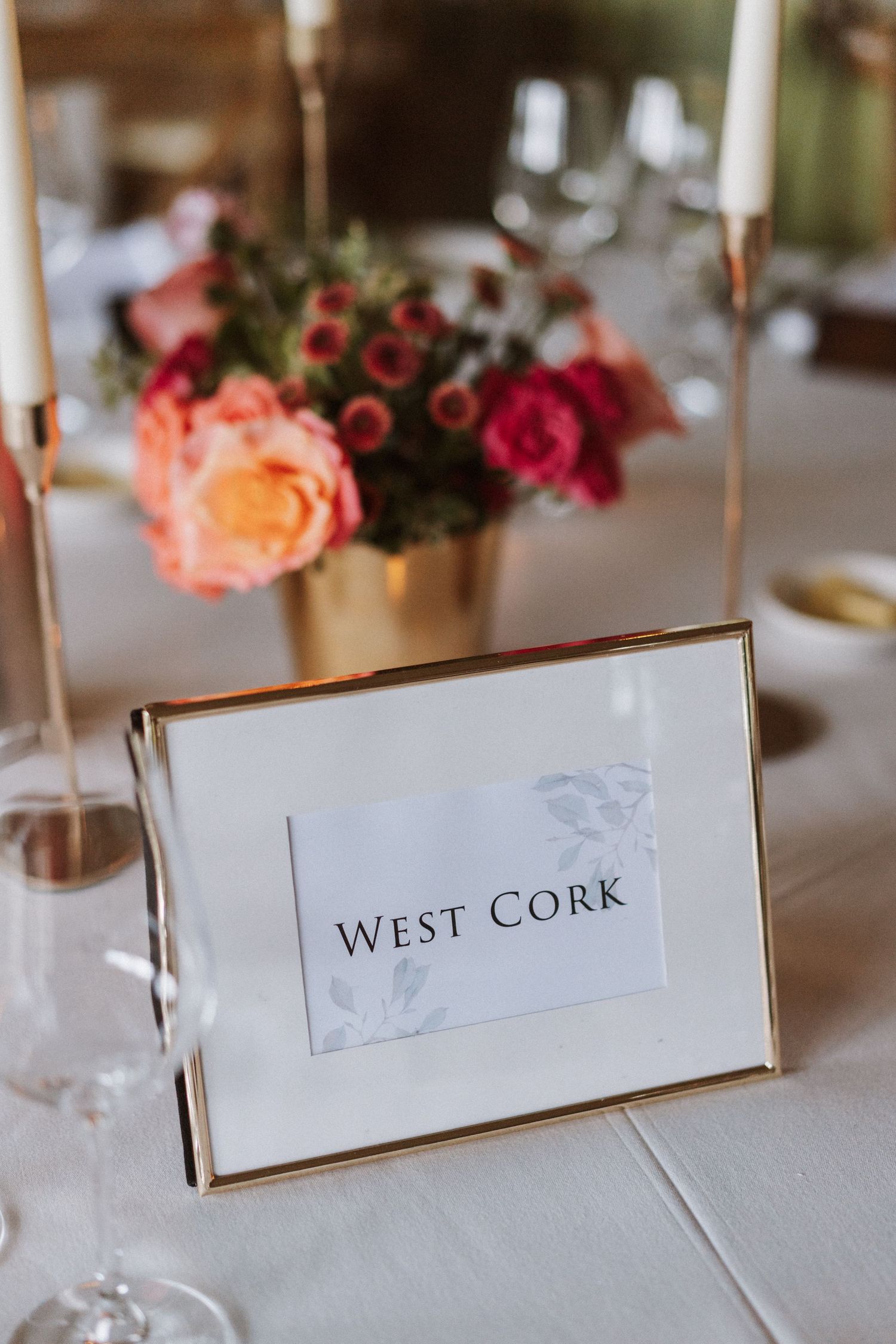 Elegant table setting with 'West Cork' sign and pink roses in gold frame at wedding reception.