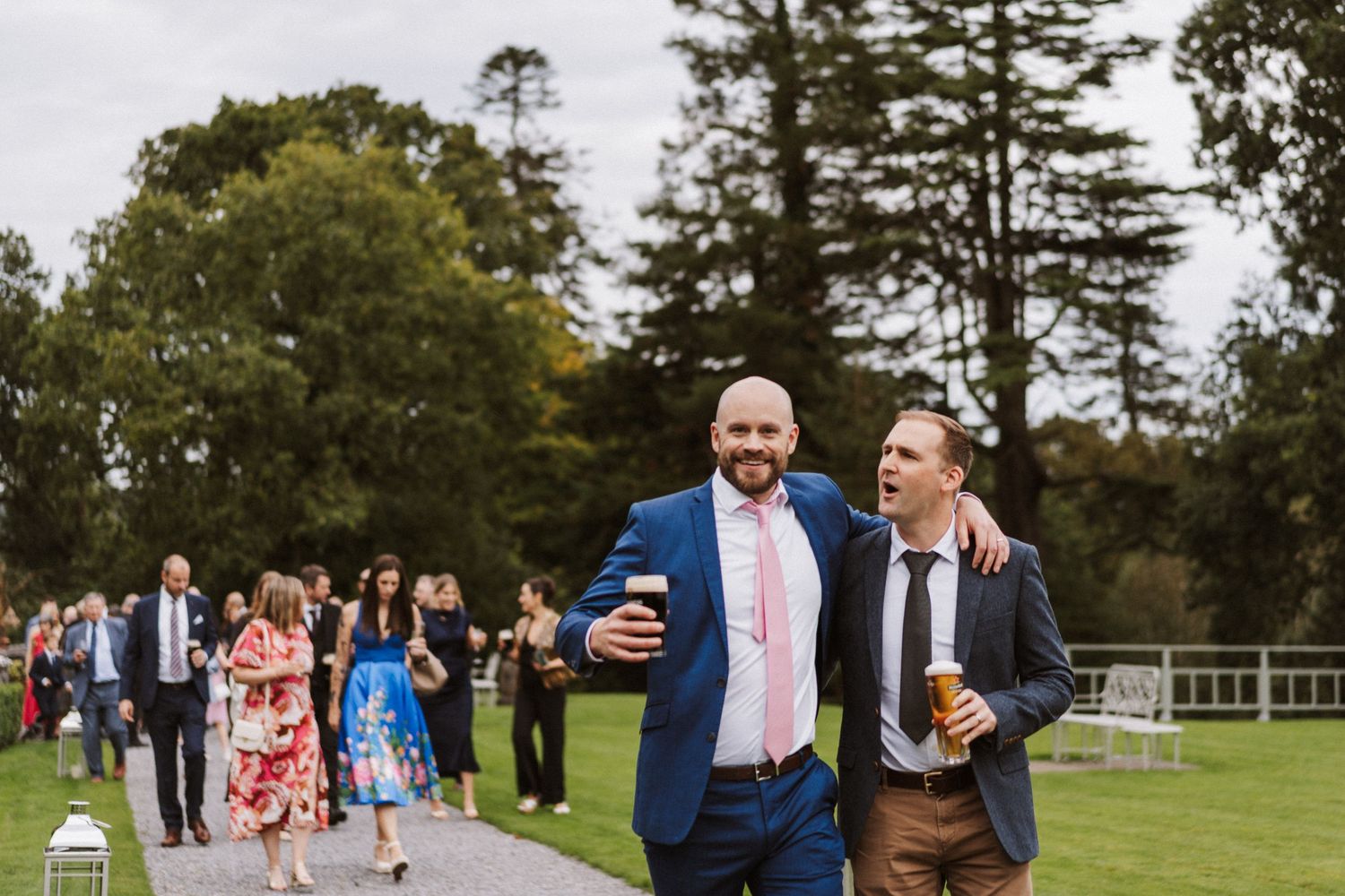 Wedding guests gather on a lush green lawn during an outdoor celebration at a country venue.