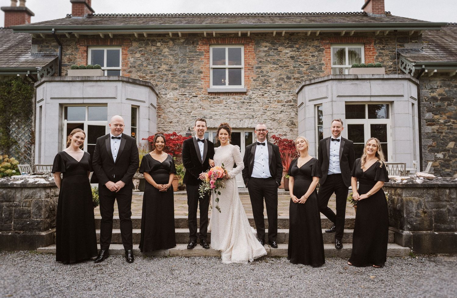 Wedding party poses together in front of rustic stone wall in a series of panoramic group shots.