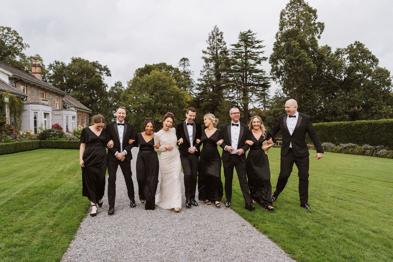 Wedding party walking and posing together on a lush green lawn at an elegant estate venue.
