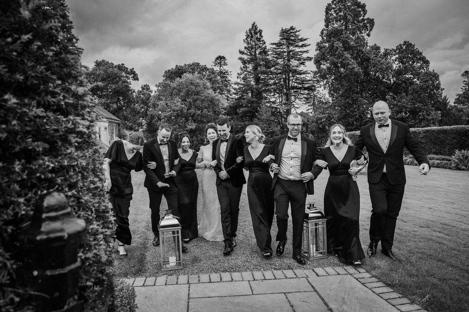 Black and white wedding party photo showing groomsmen lined up outdoors in formal attire on a garden patio.