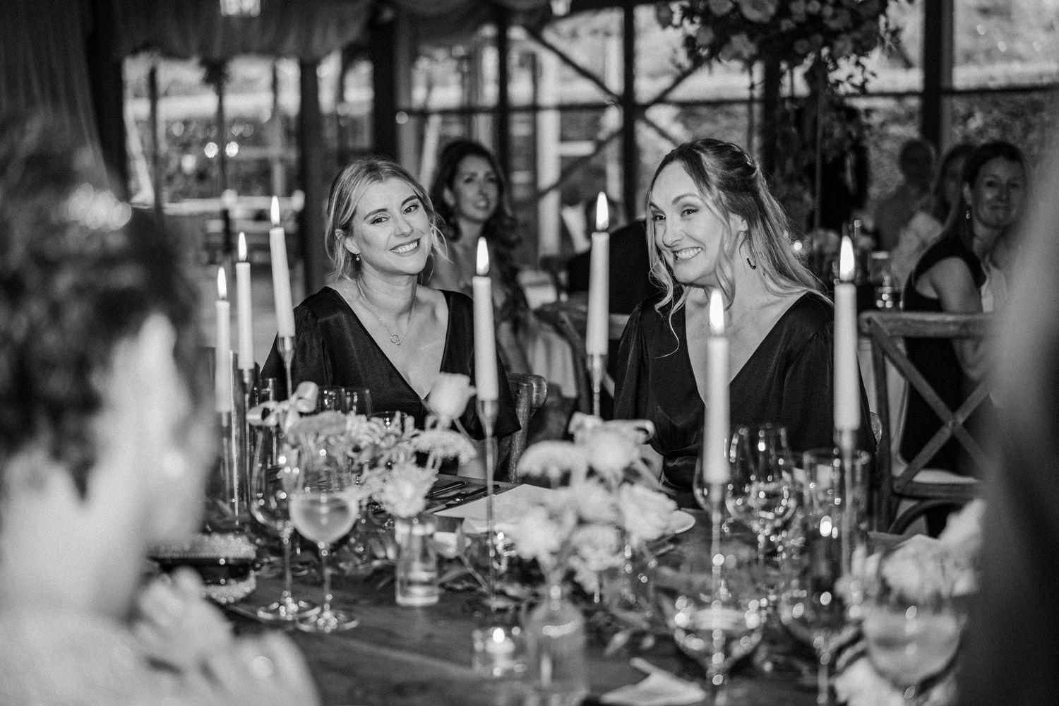 Black and white photo of guests engaged in conversation at an elegant dinner table with wine glasses and table settings.