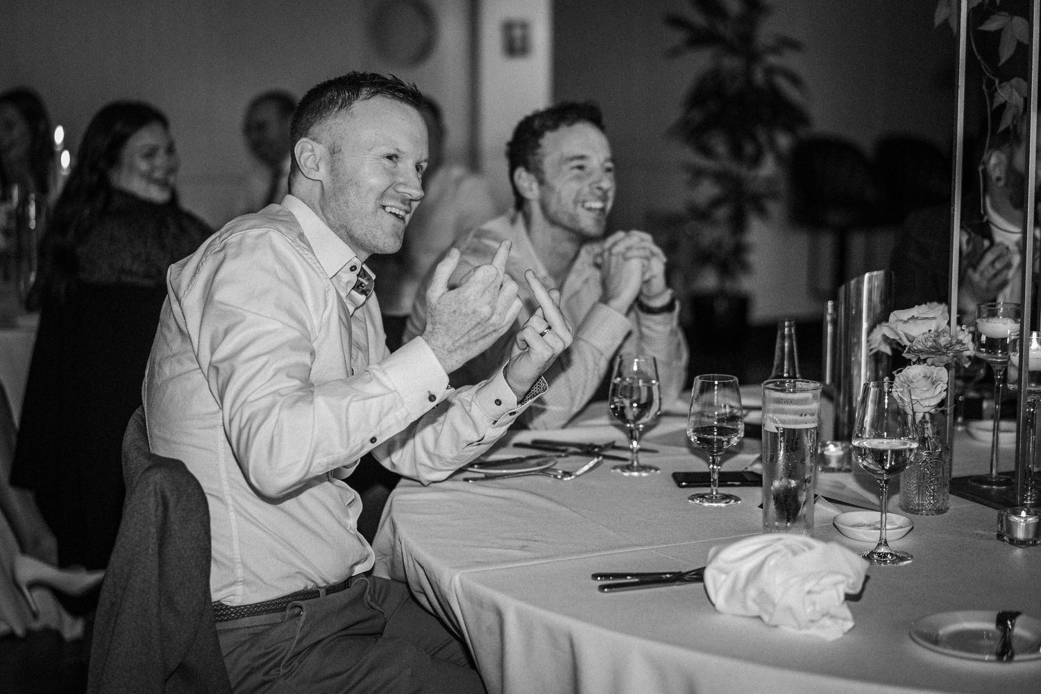 A group of people laugh and smile while dining together at a restaurant table in a black and white photograph.