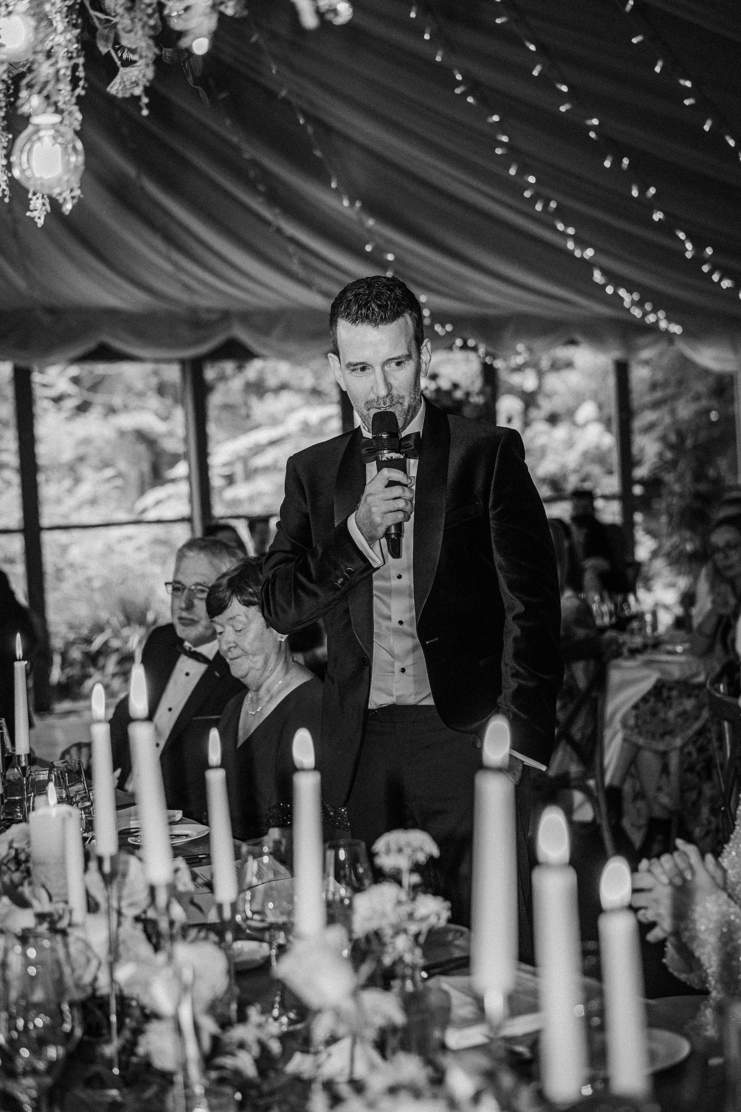 Guests at an elegant wedding reception under a draped tent ceiling with white candles and string lights creating ambiance.