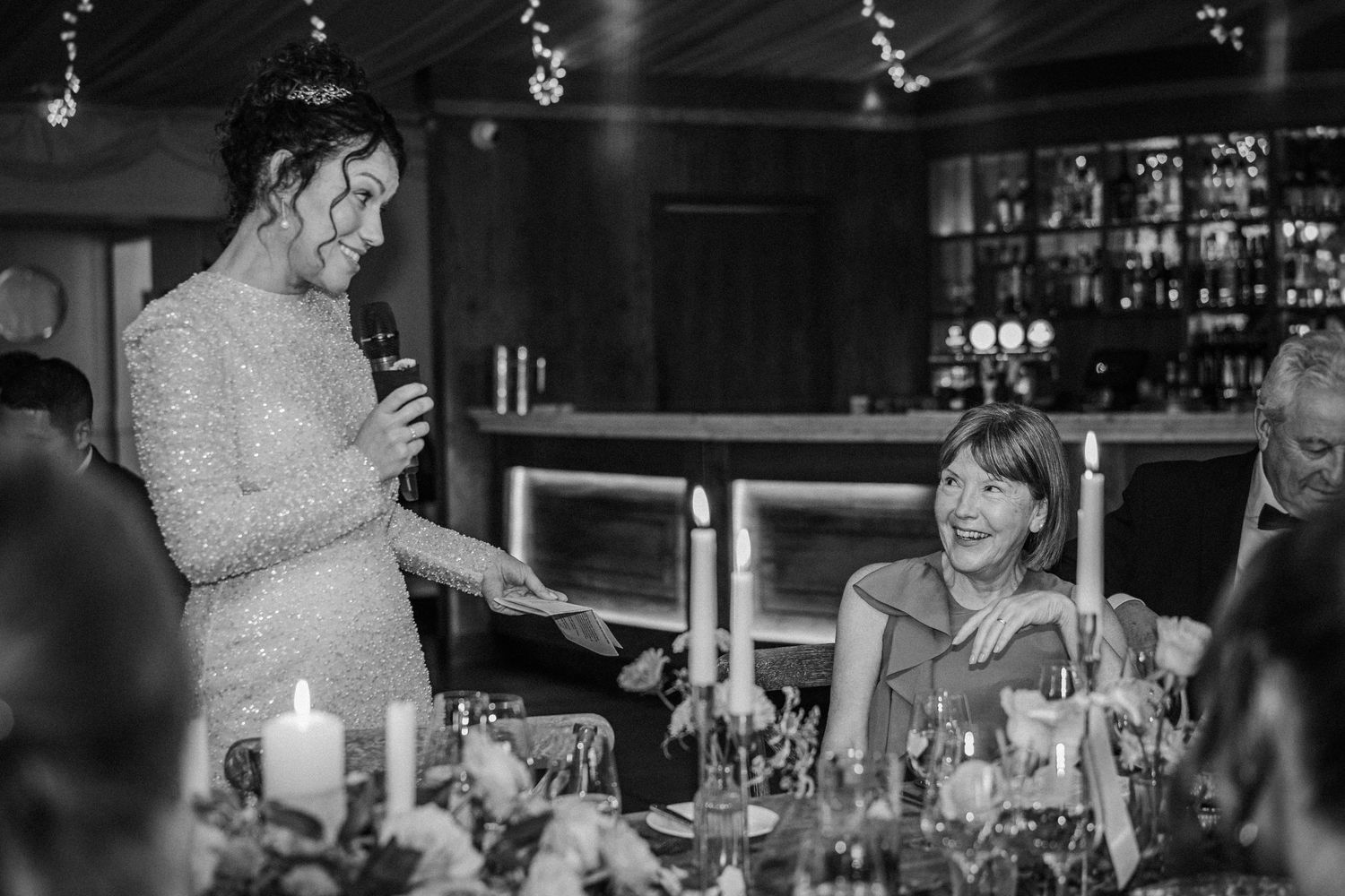 Wedding guests sharing joyful moments and laughter during speeches at an evening reception.