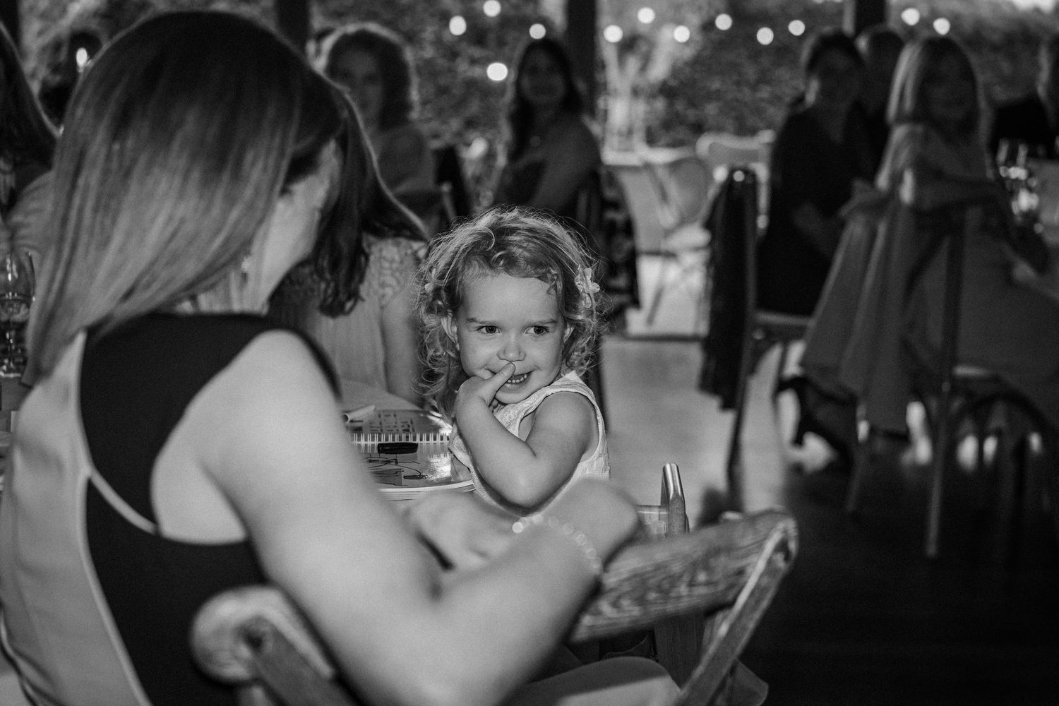 Wedding guests laughing and enjoying themselves during a reception celebration with string lights overhead.