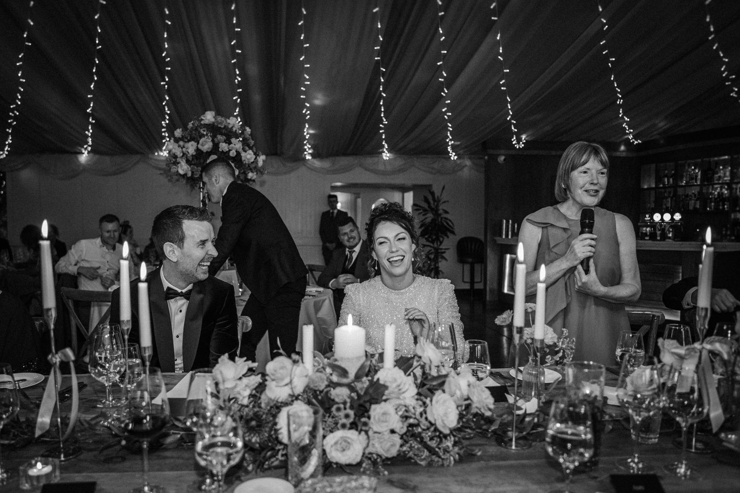 Wedding reception guests seated at decorated tables with candlelight and floral centerpieces in black and white.