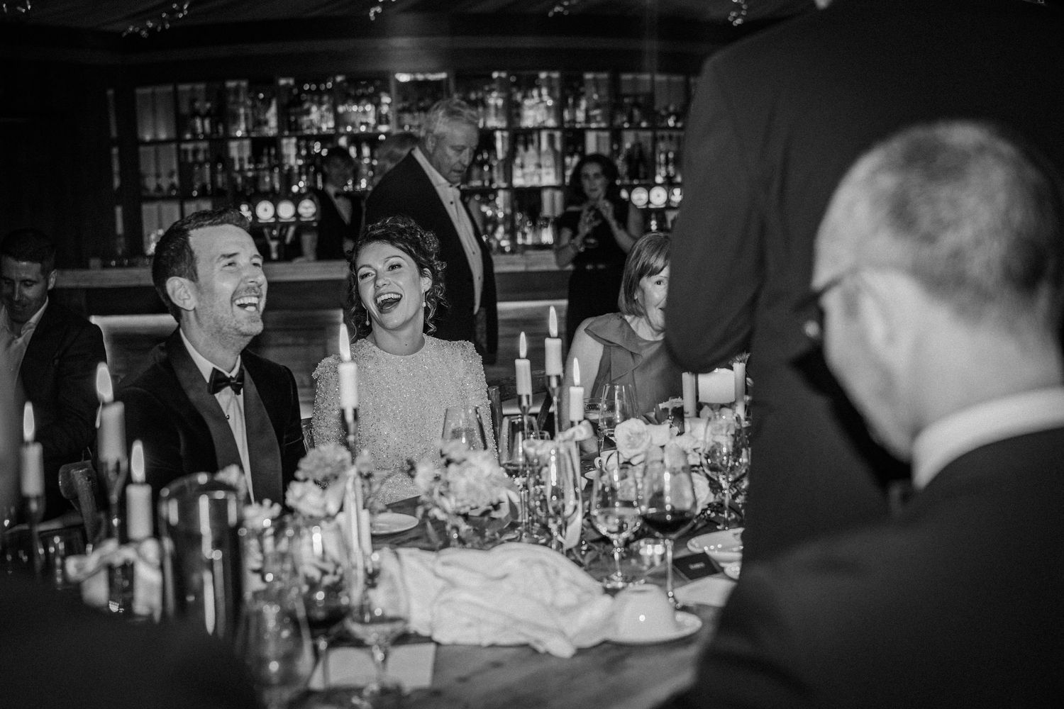 Black and white photo of wedding guests laughing and enjoying themselves at a reception dinner.