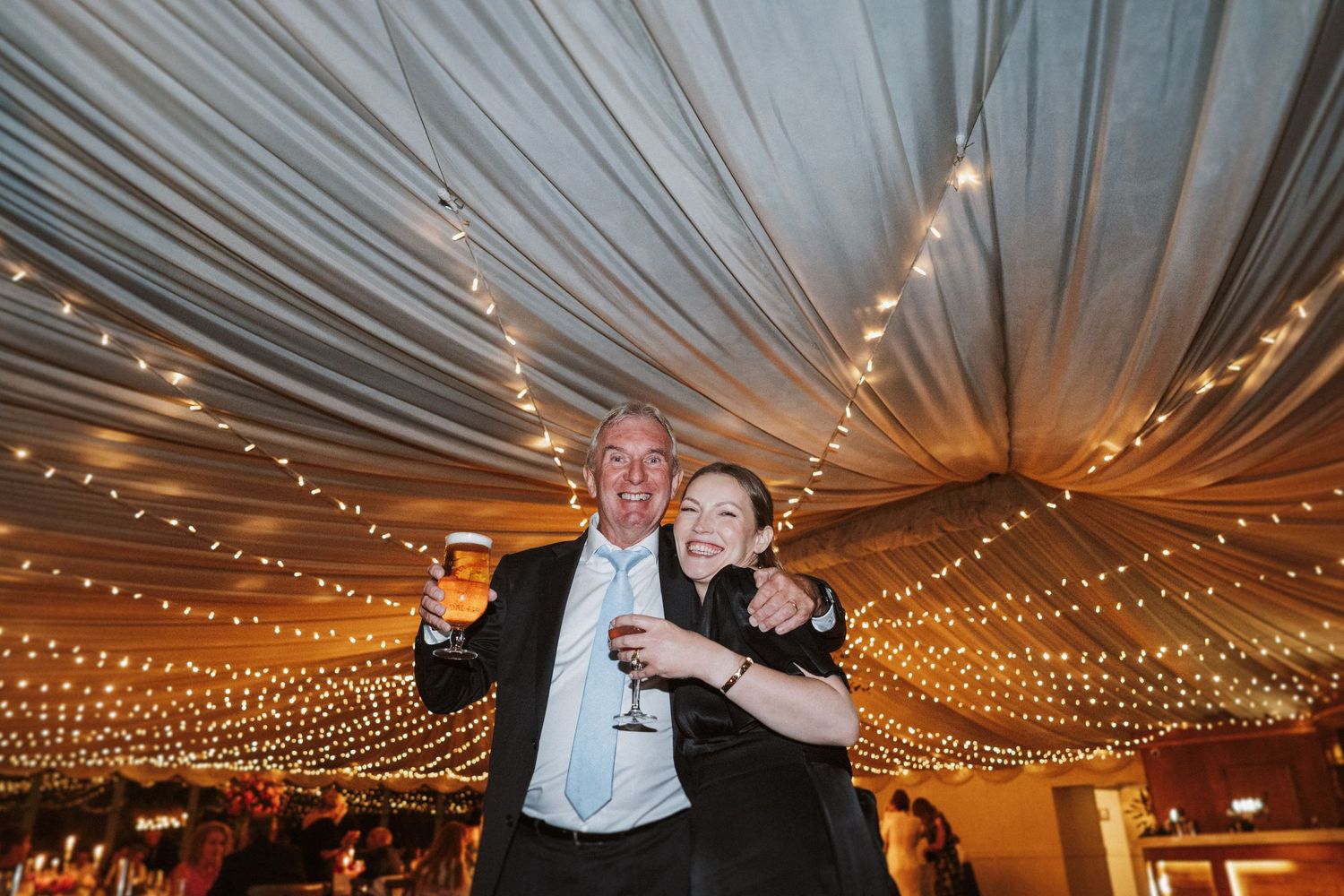 Wedding celebration under a tent with dramatic fabric draping and warm string light illumination creating a magical atmosphere.