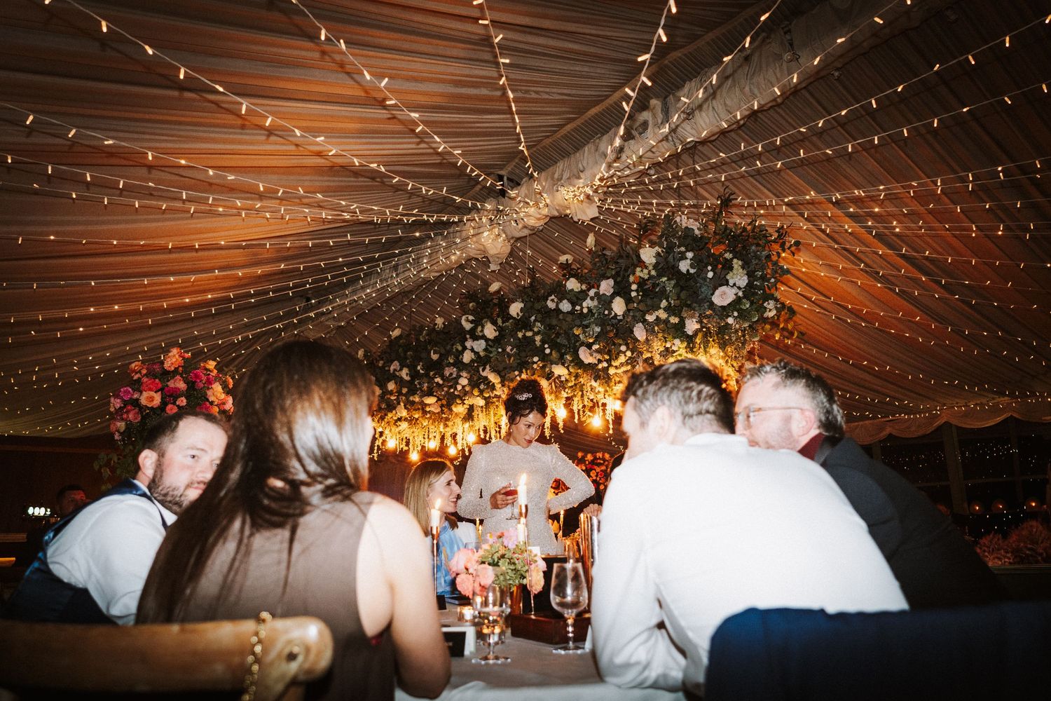 Guests dance beneath twinkling string lights at an evening wedding reception celebration.