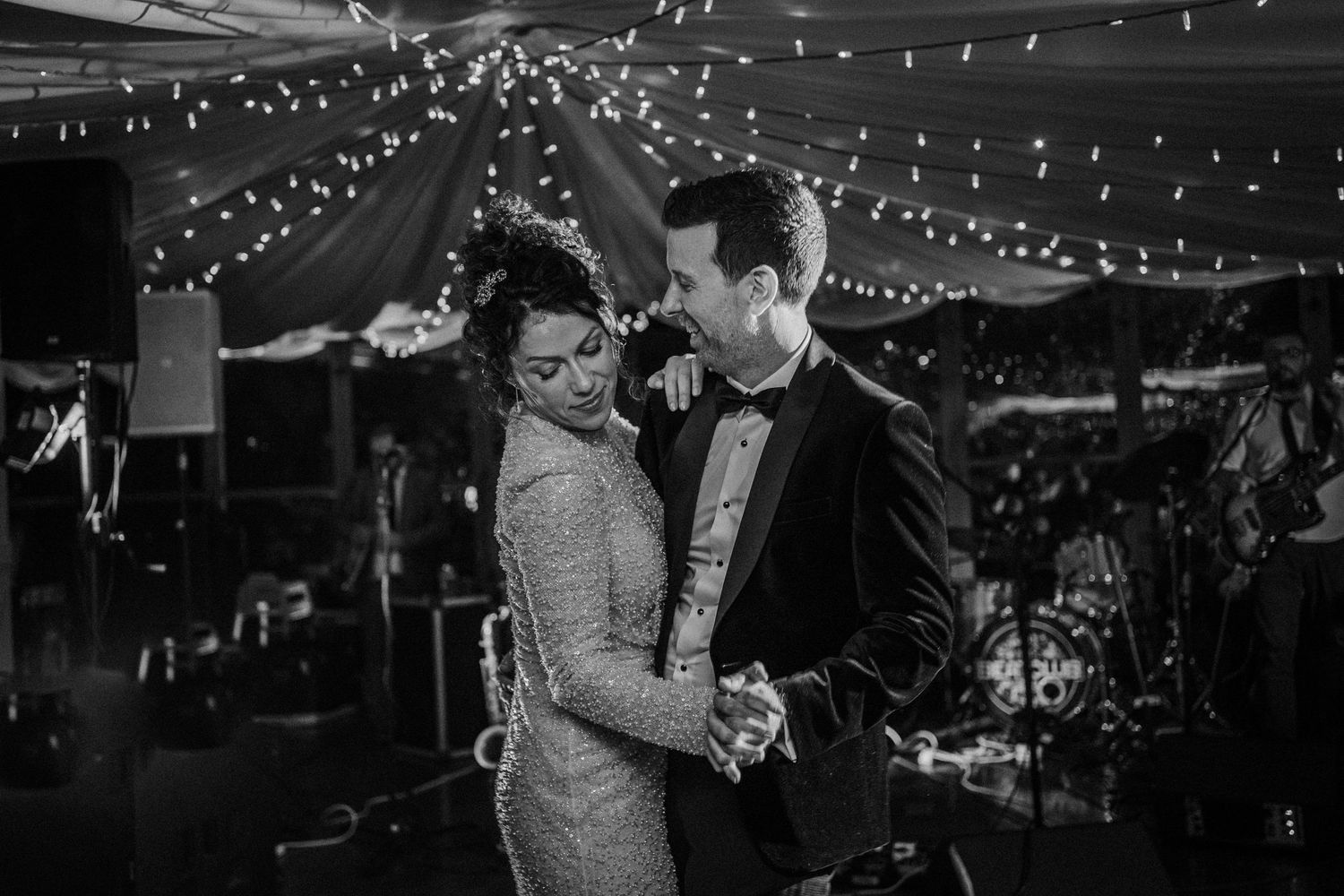 String lights illuminate a dance floor where couples are dancing at a wedding reception.