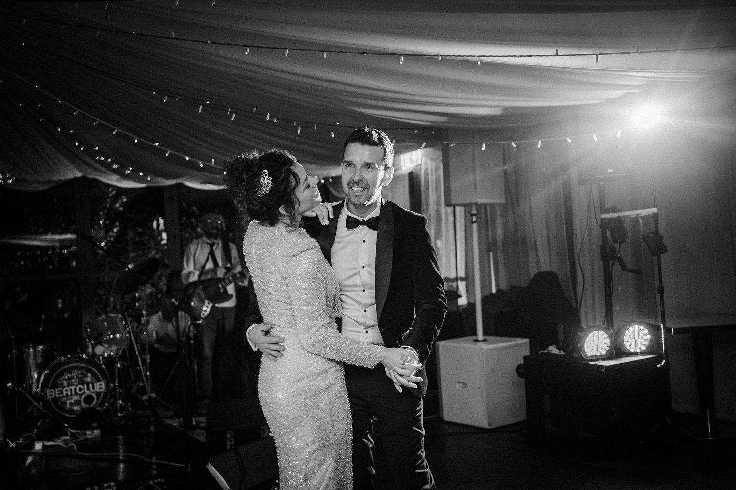 Black and white wedding reception photos show couples dancing and celebrating in an indoor venue with string lights.