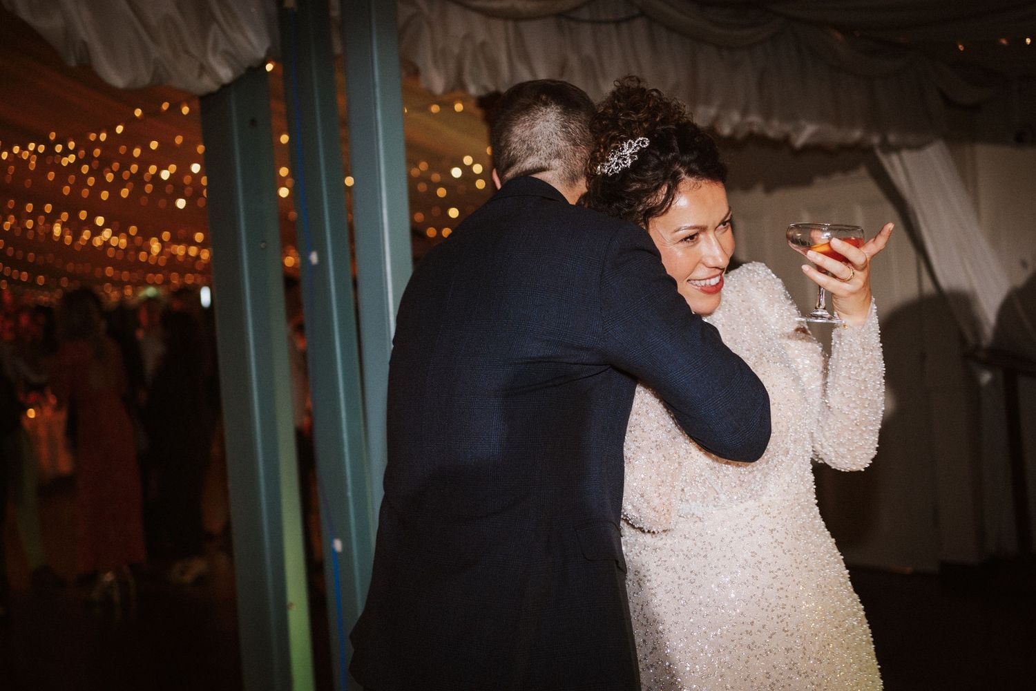 Couples dance together during an evening wedding reception under romantic string light decorations.