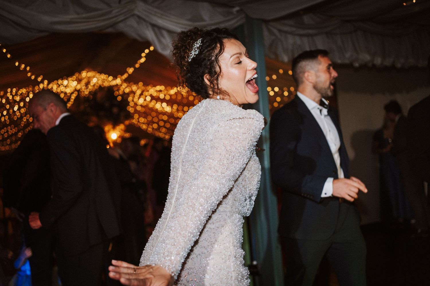 A couple dances together at an evening wedding reception under warm lighting and decorative string lights.