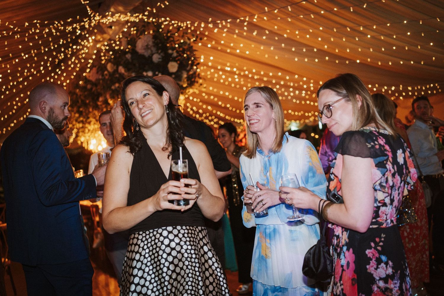 String lights create a warm ambiance at an indoor party venue with people dancing and socializing.